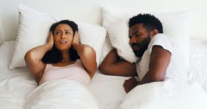 Woman in bed covering her ears because her partner is snoring from his sleep apnea.