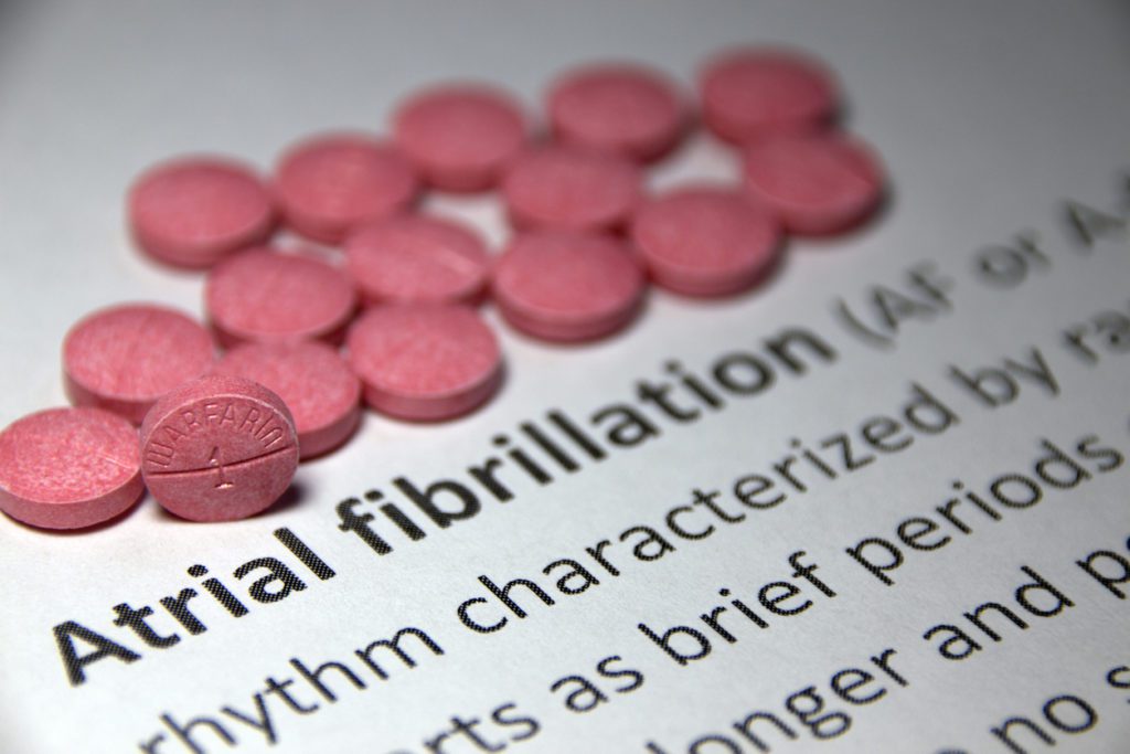 A textbook with pink pills above bolded words that say, "Atrial fibrillation".