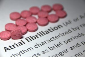 A textbook with pink pills above bolded words that say, "Atrial fibrillation".