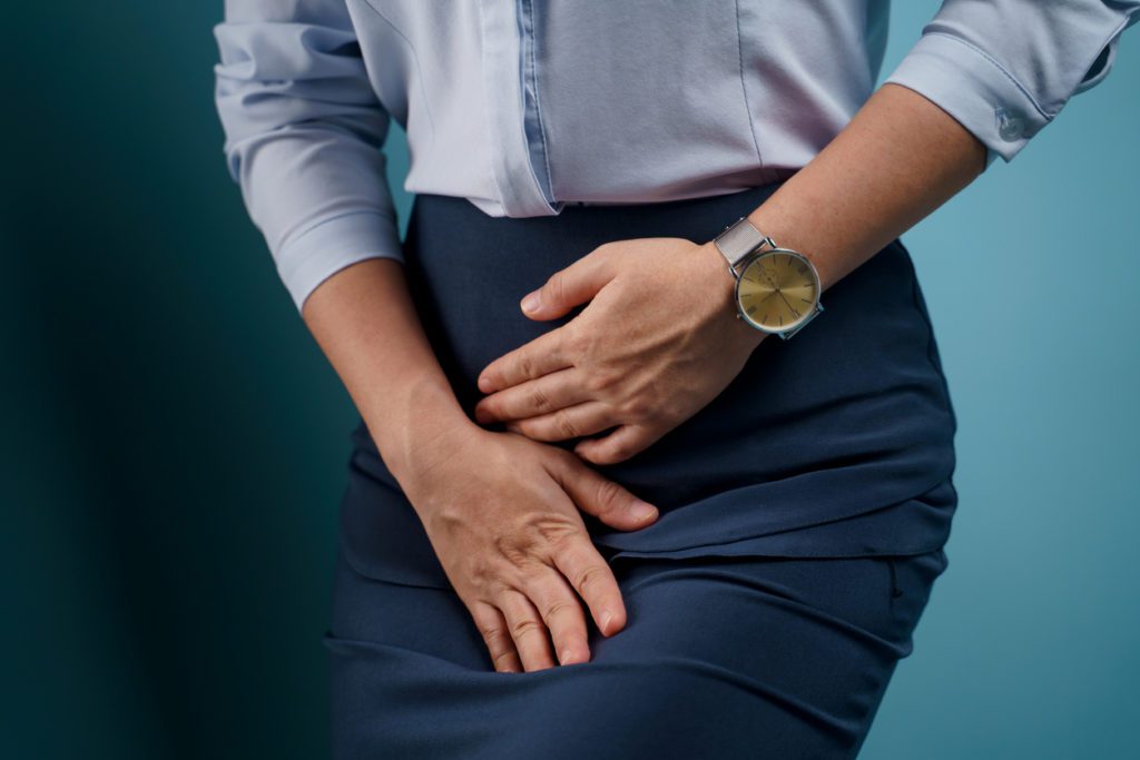 A woman sitting down and pressing against her bladder due to her painful UTI.