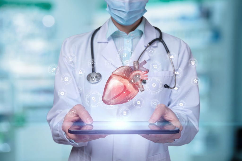 A cardiologist holding a tablet with an illustration of a heart symbol floating about it.