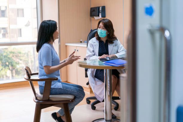 Mature patient discussing with female doctor. Medical professional listening to woman. They are sitting at desk in office.
