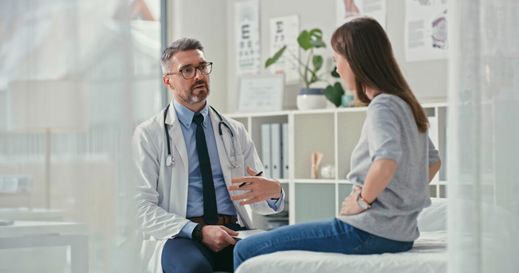 primary care doctor sitting with his patient in the clinic and asking questions during a consultation