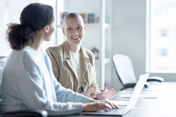 Two women smile as they discuss with one another. One of the young women has a shaved head in cancer center