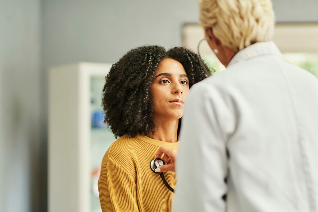 Female patient looking at primary care doctor examining her chest in clinic