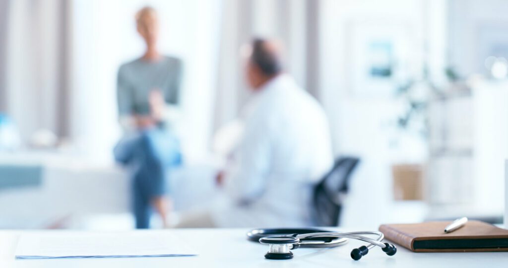 A senior male doctor consults with a senior female patient in a clinic.