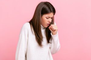 A young brunette woman is feeling unwell; she is coughing and appears to have a cold with a high fever.