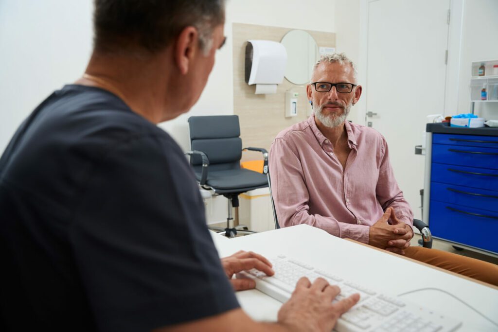 A bearded male patient with glasses is at a doctor's appointment at a primary care physician's office.