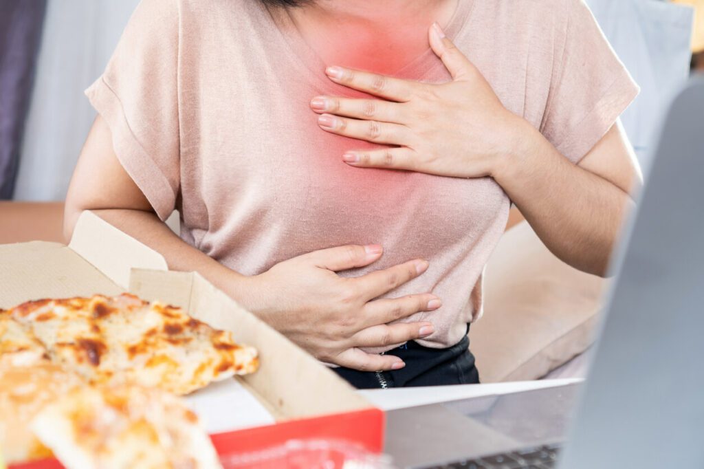 A woman is experiencing chest pain and heartburn caused by acid reflux after eating pizza.