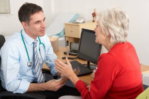 A male primary care physician (PCP) is having a conversation with a senior woman in his office.