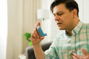 Closeup of a man managing asthma, using inhaler while resting on living room sofa.