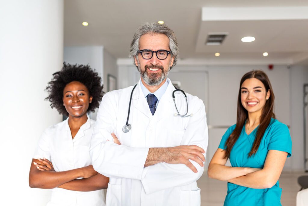 Portrait of a senior male primary care doctor with a stethoscope standing with his diverse medical team.