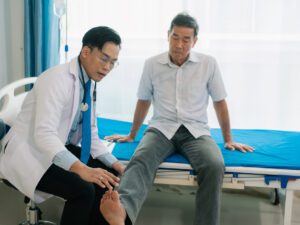 A vascular specialist examines an elderly male patient lying on a bed for Peripheral Artery Disease (PAD).