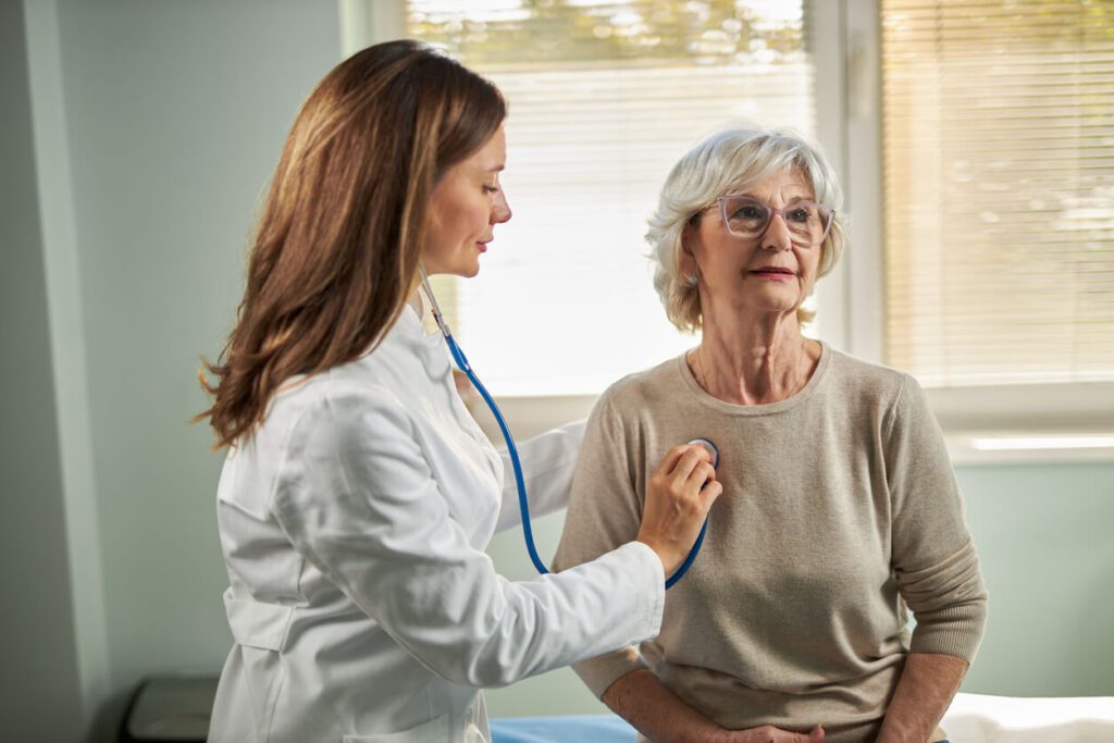 Female pulmonary specialist listening to mature woman's heartbeat in the office.