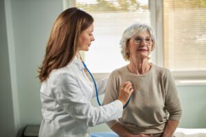 Female pulmonary specialist listening to mature woman's heartbeat in the office.
