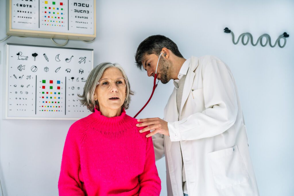 A pulmonologist is examining a senior woman with stethoscope in medical clinic.
