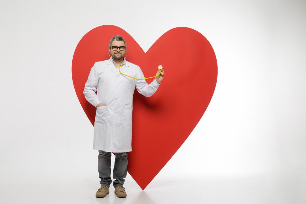 Male cardiologist (heart doctor) checking heart symbol with stethoscope for heart health awareness